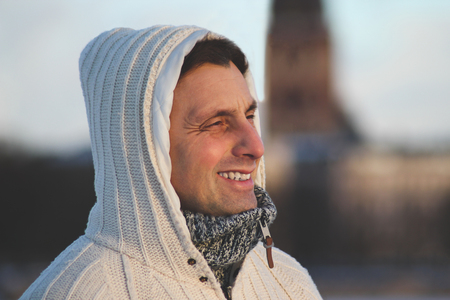 Close up portrait of a middle aged man wearing a hooded white knitting jacket in cold and windy weather and looking into the distance. Winter time in Riga, Latviaの写真素材