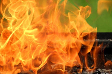 Close-up charcoal grill with orange powerful flame on green background