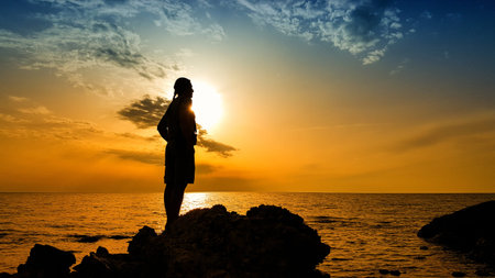 Alone man tourist standing on the stone in the sea and enjoying scenery during sunrise or sunset