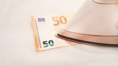 Iron smooths a bill of fifty euros. Ironing cash with hot iron for antibacterial disinfection. Clearing money. Panic and phobia  concept caused by pandemic.の写真素材