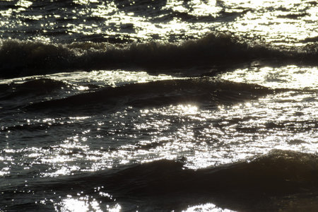 Sun glare on the water and ripples on the sea water. Black deep water with small waves close up.