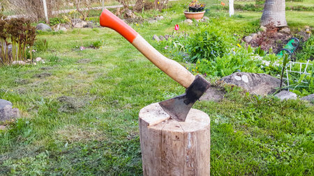 Ax stuck in the stump. Woodworking tool. Garden background. Travel, adventure, camping gear,...