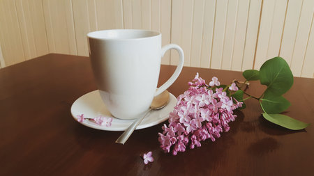White porcelain cup of coffee or tea with lilacs on the wooden table. Home decor and comfort concept.の写真素材