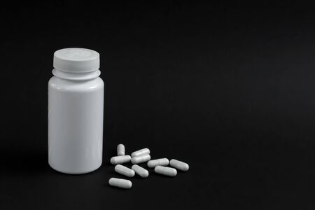 White jar with medicinal capsules on a black backgroundの写真素材