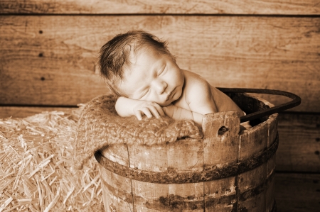 Sepia toned image of an 11 day old newborn baby boy sleeping in an old wooden banded bucket  Shot in the studio with a rustic wood background and hay bail の写真素材