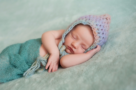 Portrait of a 13 day old sleeping newborn baby girl. She is wearing a multi-colored crocheted pixie hat and wrapped in gauzy teal colored fabric.の写真素材