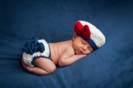 Eight day old newborn baby girl wearing a white and blue sailor costume  She is sleeping contentedly on her stomach  Shot in the studio on navy blue velvet の写真素材