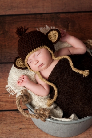 A newborn baby wearing a crocheted monkey hat and sleeping in a galvanized bucket  Shot in the studio with a rustic wood background の写真素材