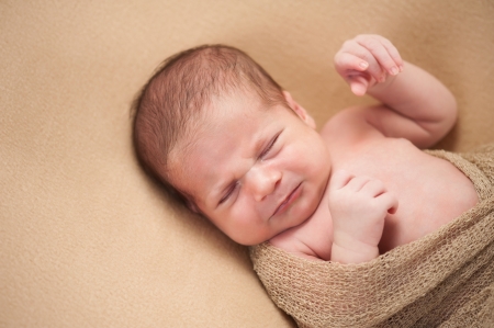 A 3 week old, fussy newborn baby boy  Shot in the studio on a beige blanket の写真素材