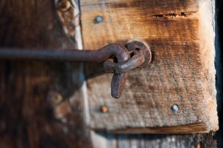 A close-up shot of a closed rusty, antique, hook and eye latch located on the door of an old wooden outbuilding の写真素材