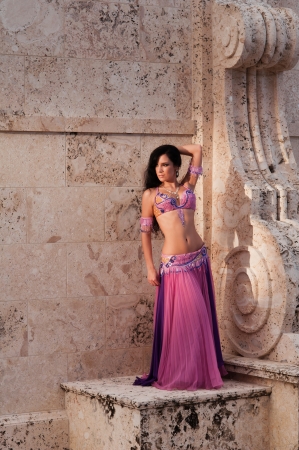 A full length shot of a beautiful belly dancer wearing a pink costume and posing on a stone structure with Mediterranean style design elements.の写真素材