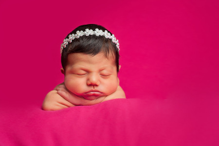 A beautiful 8 day old newborn baby girl wearing a fancy rhinestone headband  Shot in the studio on a hot pink background の写真素材