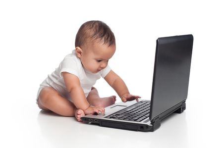 A portrait of a seven month old, hispanic baby boy typing on a laptop computer  He is wearing a onesy and there is motion blur where his hand is moving to touch the keyboard  Shot in the studio and isolated on white の写真素材