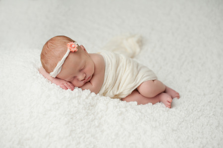 Portrait of a red headed, 2 week old, newborn baby girl  She is wrapped in white material and sleeping on a white, gauzy blanket の写真素材