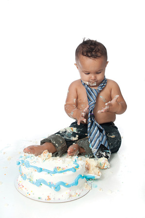 A one year old boy making a mess of his birthday cake. Shot in the studio on a white background.の写真素材