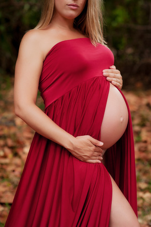 A closeup shot of a pregnant woman's belly. She is wearing a red maternity gown that exposes her baby bump.の写真素材