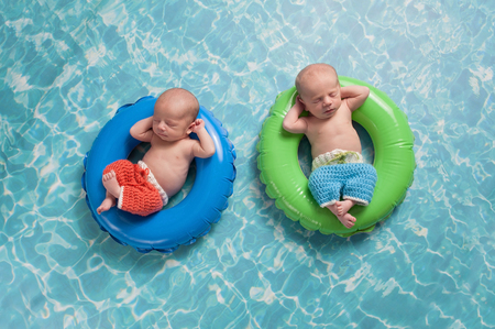 Four week old twin, newborn, baby boys wearing crocheted board shorts and sleeping on a tiny inflatable swim rings. Shot in the studio on a background to look like swimming pool water. Four week old twin, newborn, baby boys wearing crocheted board shorts and sleeping on a tiny inflatable swim rings. Shot in the studio on a background to look like swimming pool water.