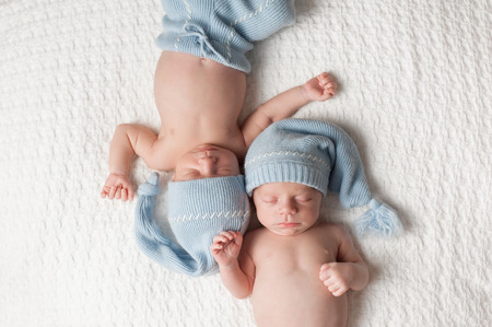 One month old fraternal, twin baby boys wearing light blue stocking caps and sleeping on a white blanket.の写真素材