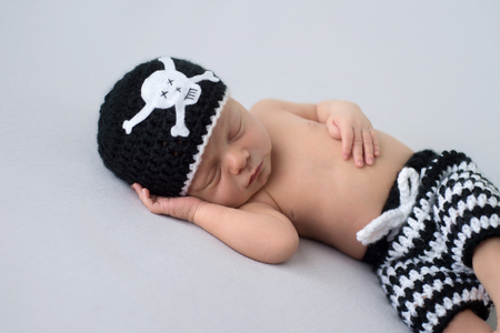 Ten day old, sleeping, baby boy wearing a crocheted, black and white, pirate inspired, skull beanie and striped shorts.の写真素材