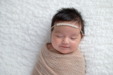 Smiling one month old baby girl swaddled in a beige wrap. Shot in the studio on a white blanket.の写真素材