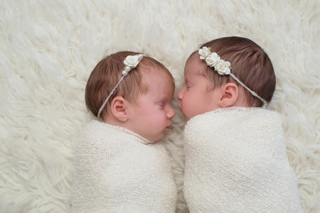 Profile headshot of two fraternal twin newborn baby girls sleeping and swaddled in white.の写真素材