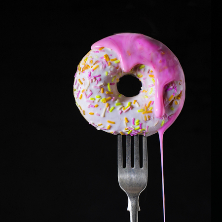 Sweet donut with white and pink glaze on a fork on a black backgroundの写真素材