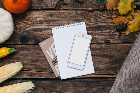 Autumn vegetables: mobile phone with white empty screen, pumpkins and corn with yellow leaves on a...