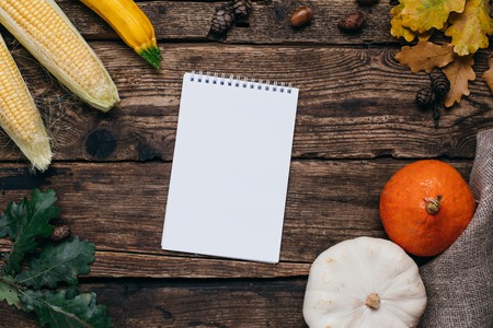 Autumn mood: white notebook, pumpkins and corn with yellow leaves on a wooden background topn viewの写真素材