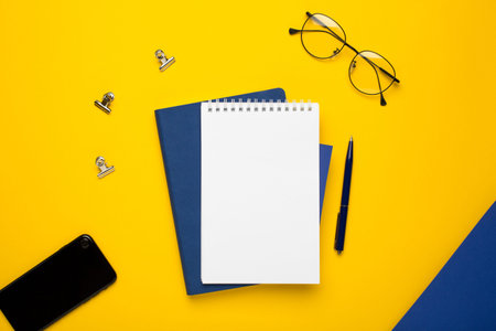 White notepad with blue notebook,pen and mobile phone on yellow background