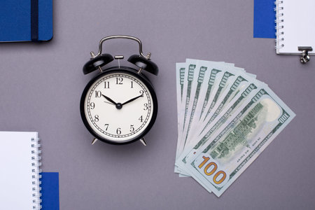 Business items - white notebook, blue notebook, alarm clock and money on a gray background