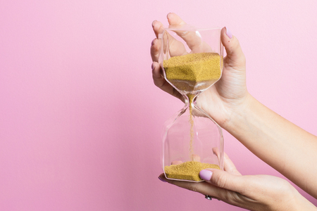 The female hand holds a sand-glass on a pink background side viewの写真素材