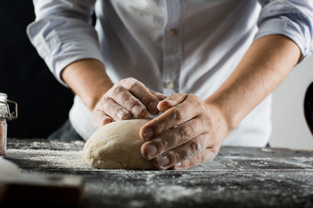 Cook kneads dough with flour on kitchen table side viewの写真素材