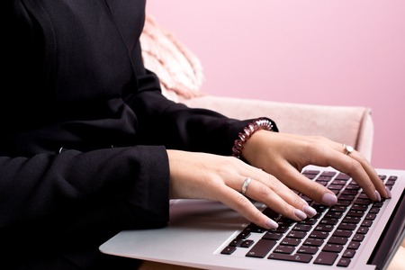 Girl with blond hair works on a laptop in a pink room side viewの写真素材