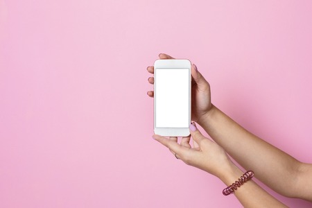Female hands hold mobile phone with white screen on a pink background side viewの写真素材