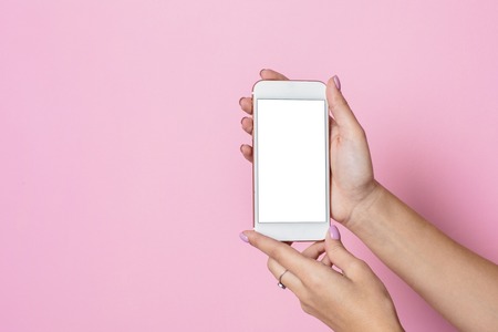 Female hands hold mobile phone with white screen on a pink background side viewの写真素材