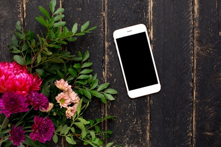 Mobile phone and bouquet of flowers on a black wooden backgroundの写真素材