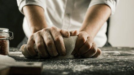 Male chef hands knead dough with flour on kitchen table side view