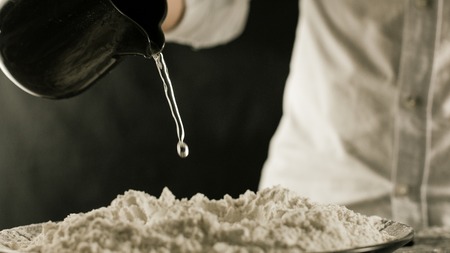 The cook pours water on the flour from the jug in the kitchen side viewの写真素材
