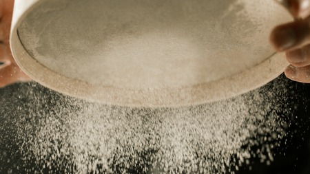 Flour sieve in male chef hands in the kitchen side viewの写真素材