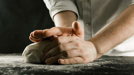 Male chef hands knead dough with flour on kitchen table side viewの写真素材