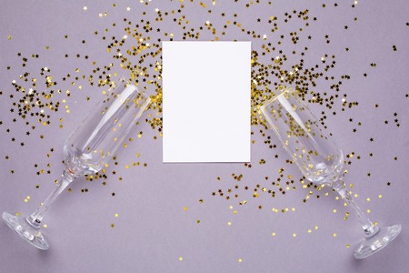 Champagne glasses with golden stars confetti and white card on gray color paper background minimal style top viewの写真素材