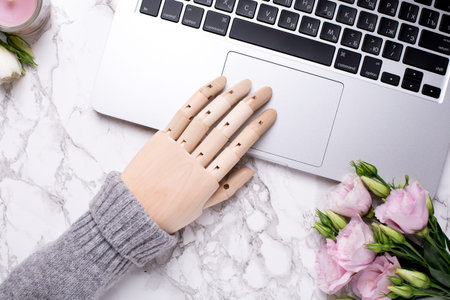 Wooden hand and laptop on marble office table with pink flowersの写真素材