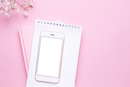Mobile phone mock up and white flowers on pink pastel table top view in flat lay style. Woman working desk background.の写真素材