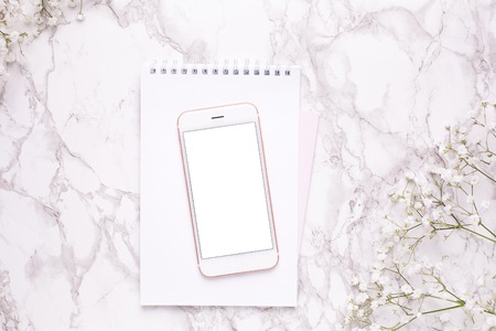 Mobile phone mock up and white flowers on marble table top view in flat lay style. Woman working desk .の写真素材