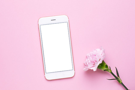 Mobile phone mock up and pink flower on pink pastel table in flat lay style. Woman working desk.の写真素材