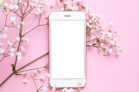 Mobile phone mock up and white flowers on pink pastel table in flat lay style. Woman working desk.の写真素材