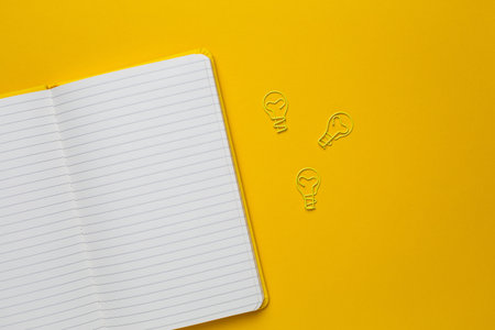 Notebook with blank pages and paperclip light bulb idea on yellow background top viewの写真素材
