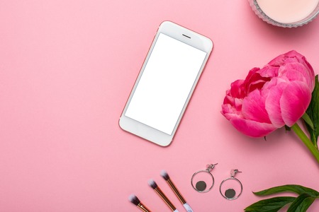 Mobile phone mock up with makeup brushes ,earrings and flower peony on pink pastel table in flat lay style. Woman beauty desk.の写真素材