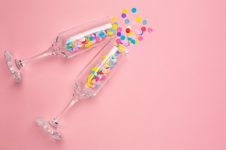 Champagne glasses with multi-colored confetti on pink color paper background . Flat lay composition for birthday, mother day or weddingの写真素材