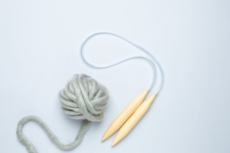 Circular knitting needles and thick grey yarn on blue background top vieww